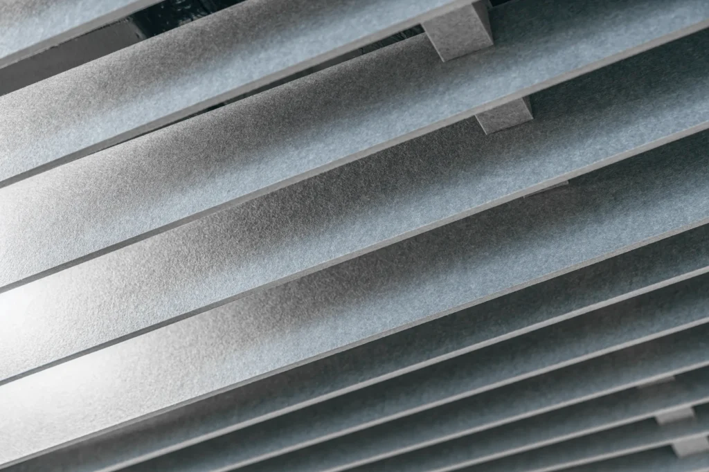 A close-up of the structure of a suspended acoustic ceiling consisting of parallel, elongated panels made of gray felt.