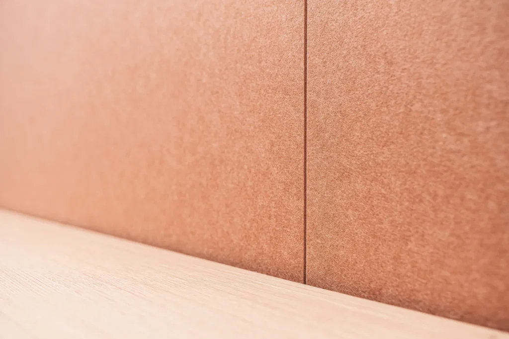 A close-up of smooth acoustic felt wall panels in brick-red or rust-red, meeting a light-colored wooden countertop.